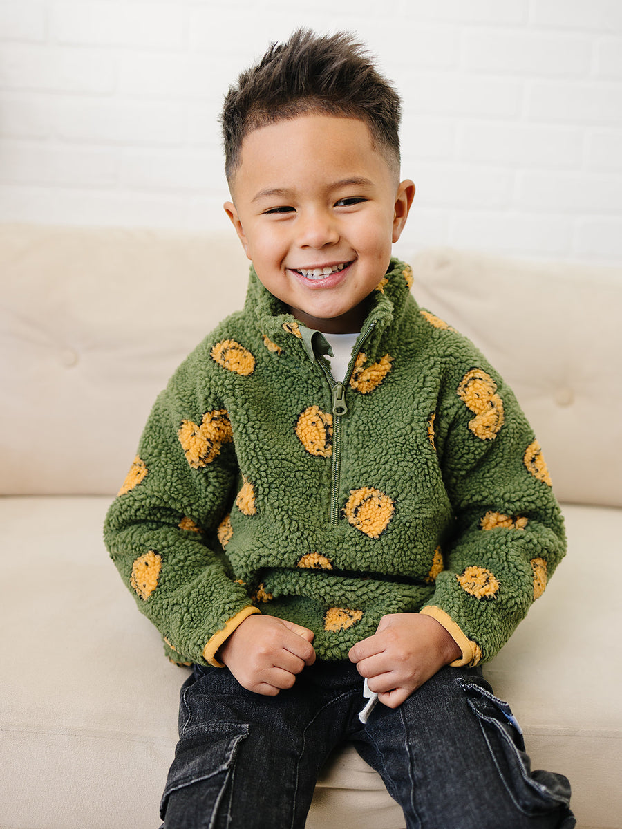 Child wearing a green sweater with yellow patterns sitting on a white couch.