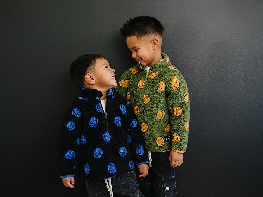 Two children wearing patterned jackets standing against a dark background